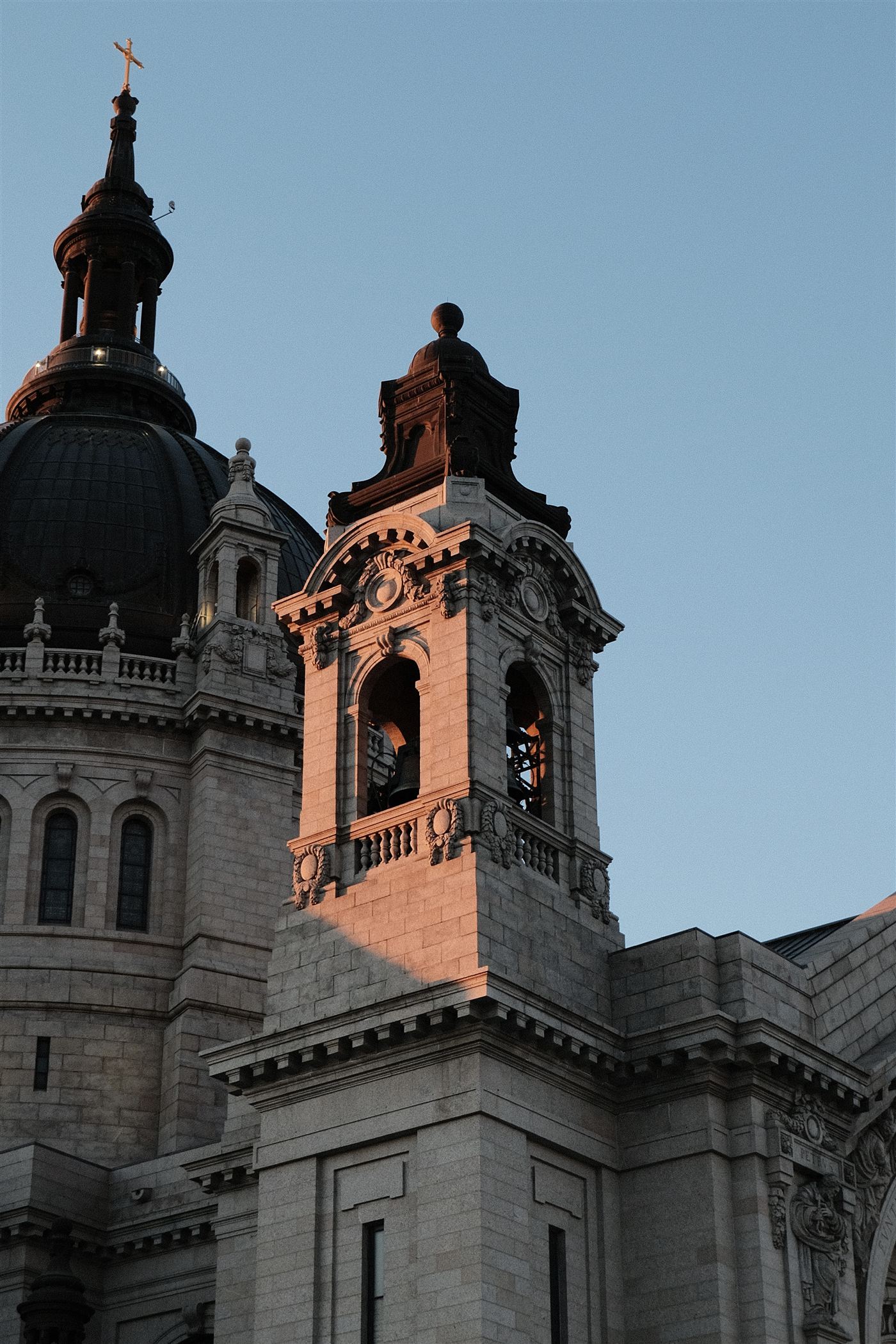 A carved stone bell tower and dome glowing in late-day light against a blue sky