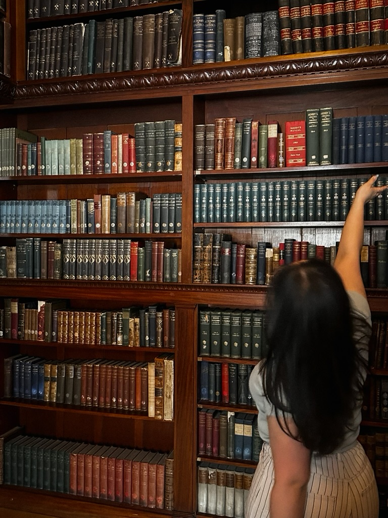 A woman reaching for a book on a tall wall of antique leather-bound volumes