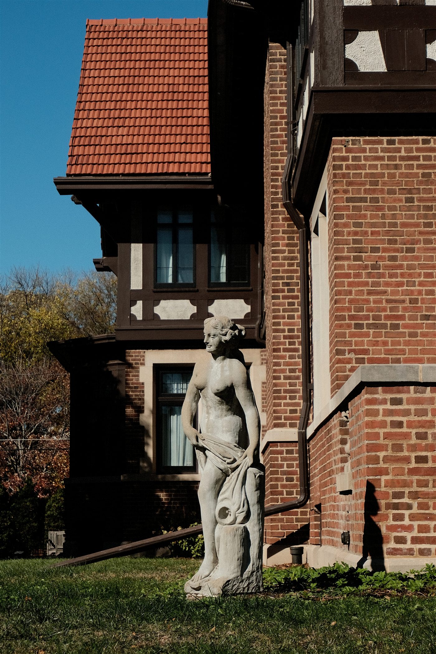 A stone statue on a lawn beside a brick and timber Tudor-style house